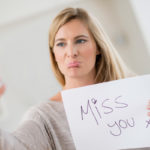 Frau mit "Miss you"-Schild und Smartphone