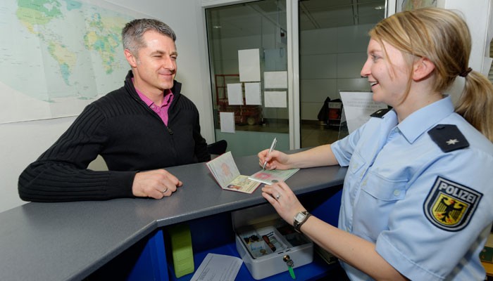 Mann zeigt seinen Pass einer Beamtin von der Bundespolizeidirektion München