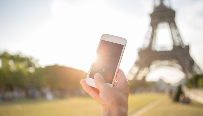 Hand mit Smartphone vor Eiffelturm