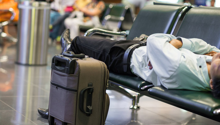 Mann im Anzug liegt auf Sitzbank im Flughafen; Foto: iStock.com/ SamuelBrownNG