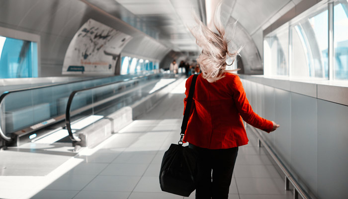 Frau mit wehendem Haar läuft über Rolltreppe am Flughafen; Foto: iStock.com/stock_colors