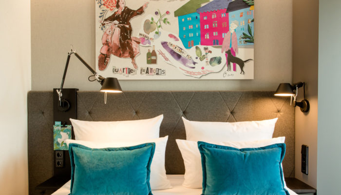 Coole Kunst über dem Bett: Blick in ein Zimmer im neuen Motel One München-Haidhausen. Foto: Motel One