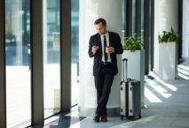 Geschäftsmann Warten Kaffeebecher to goiting for flight with his trolley suitcase in airport
